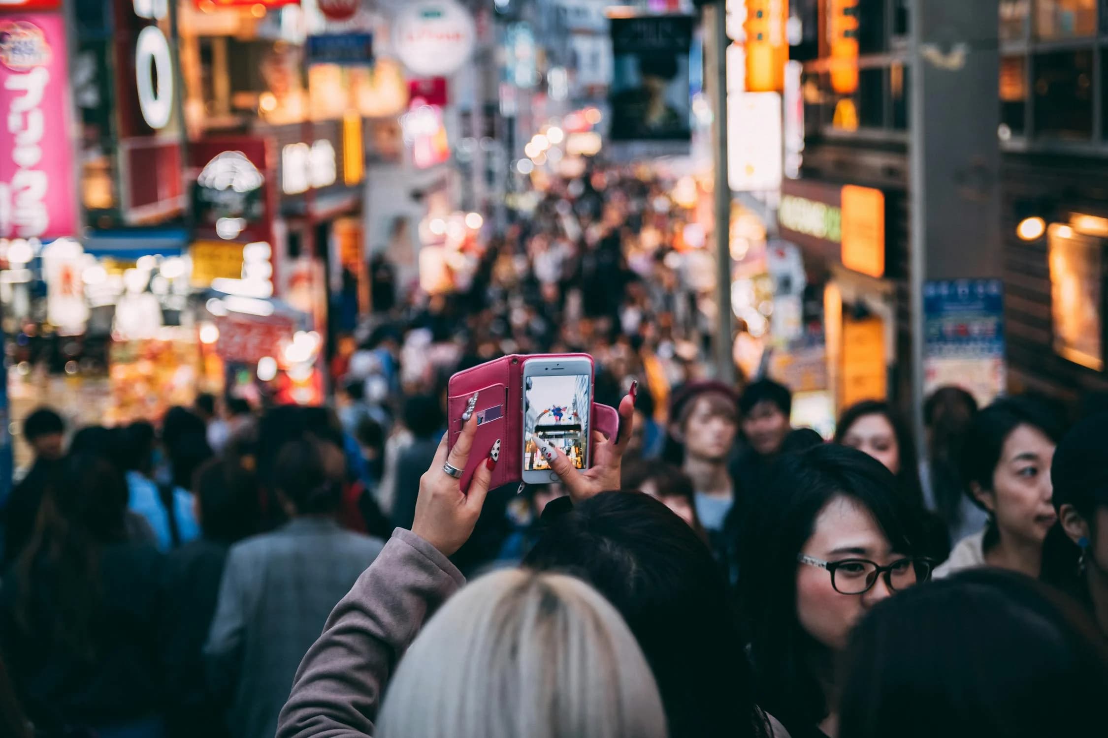 A woman taking a photo in a busy street while other people are rushing